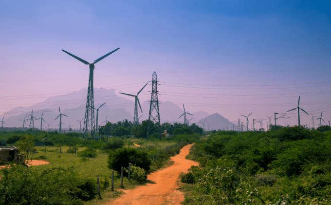Wind turbines in India stand on a plain. Mountains rise in the background.