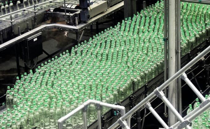 Clear glass bottles with green caps on industrial conveyor belt in factory in Siegsdorf, Germany