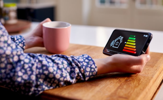 A hand holds a mobile phone, looking at a graph of energy efficiency for their home. Their other hand holds a mug.
