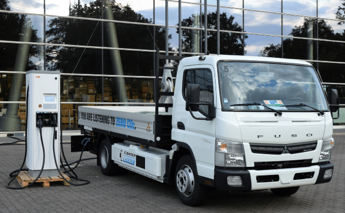 A white electric truck charging with glass windows in the background.