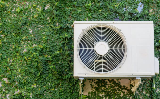 Heat pump fan mounted on wall covered with green leaves