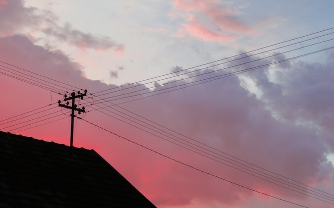 Power lines above a house against colorful sunset.